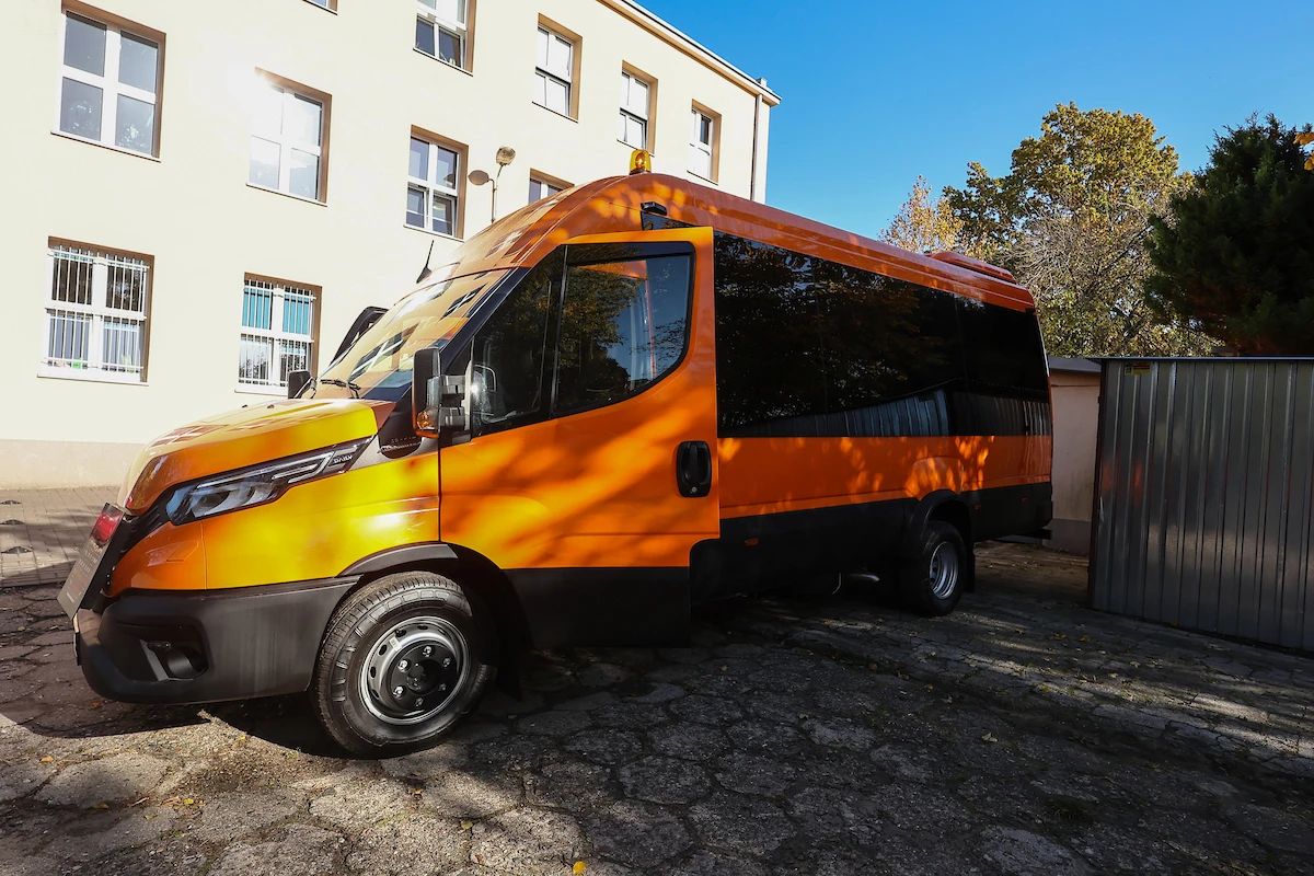 Nowy pomarańczowy autobus szkolny przed budynkiem ośrodka